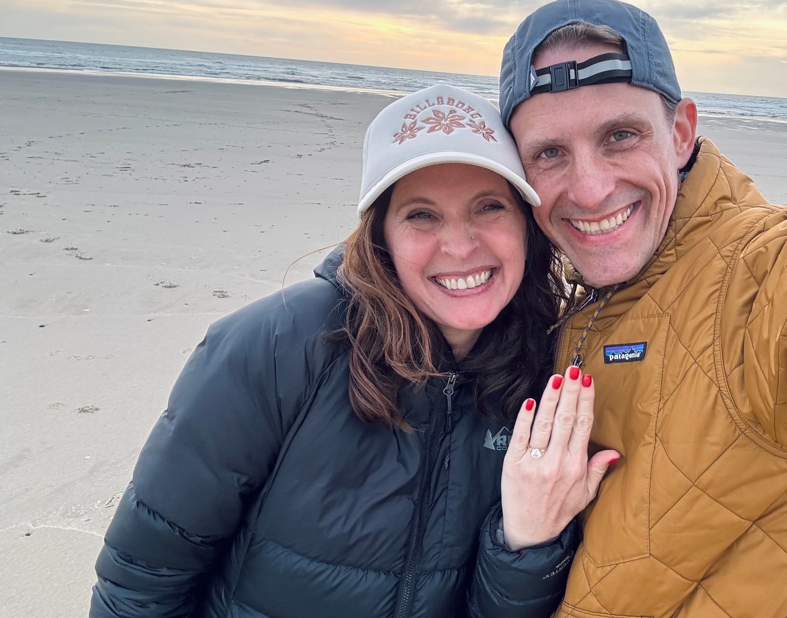 Jarod and Rachel smiling together on the beach and showing Rachel's engagement ring